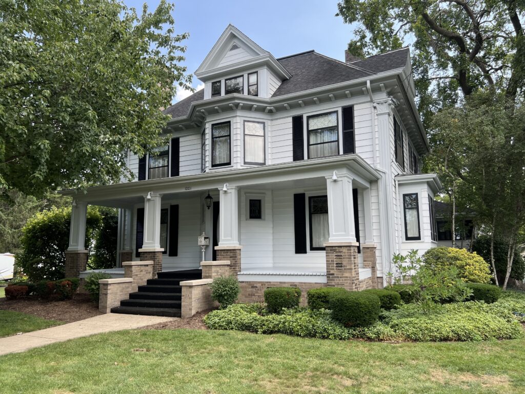 Elegant white Victorian-style house with black shutters, landscaped garden, and stone steps, showcasing a completed exterior painting project by Trusted Painters LLC.
