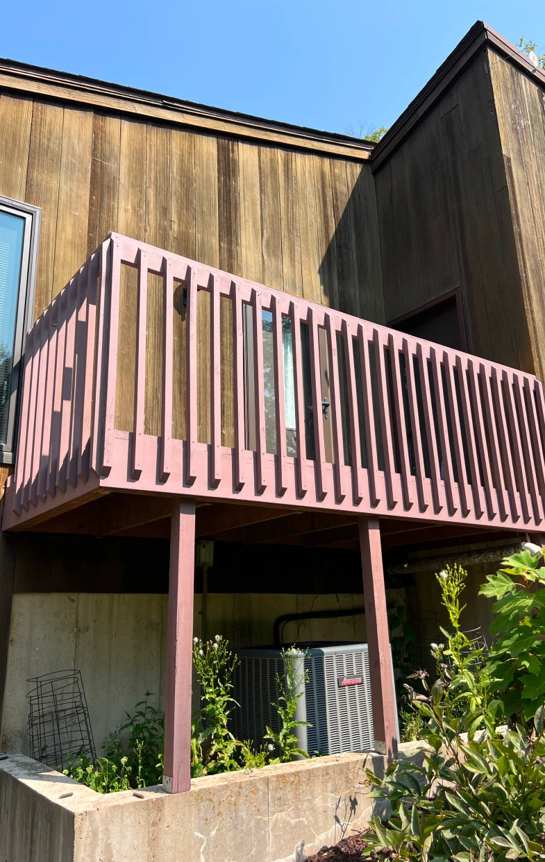 Deck with freshly painted pink railing and adjacent weathered wood wall, showcasing the results of professional deck refinishing services by Trusted Painters LLC in Rockford, IL.
