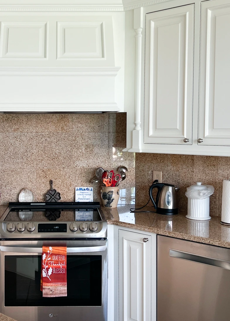 Modern kitchen featuring freshly painted white cabinetry, stainless steel appliances, and a granite countertop, showcasing a decorative towel with the words "Grateful, Thankful, Blessed" for a warm, inviting atmosphere.