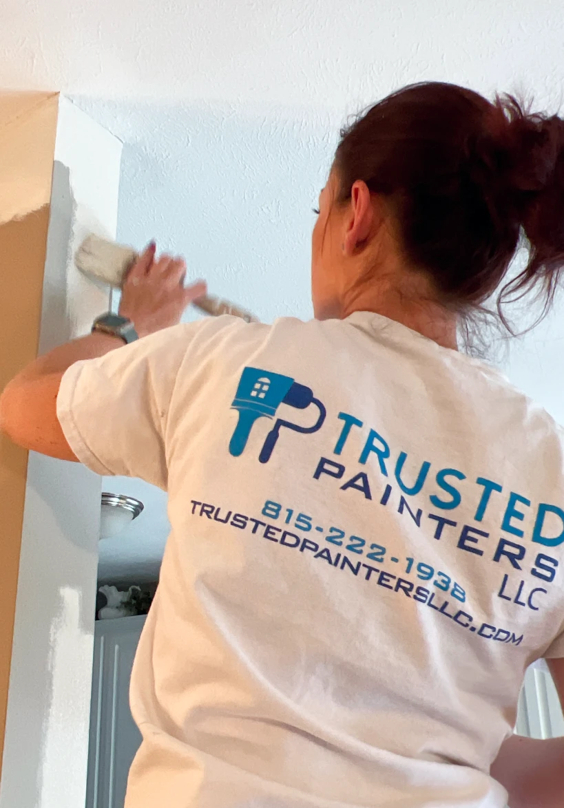 Painter applying primer or paint to a wall, wearing a Trusted Painters LLC shirt, demonstrating professional cabinet painting services in a home setting.