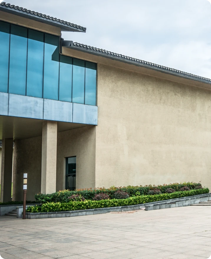 Modern commercial building exterior with large glass windows and textured stucco wall, featuring landscaped greenery and a stone pathway, illustrating professional painting and maintenance for enhanced curb appeal and property value.